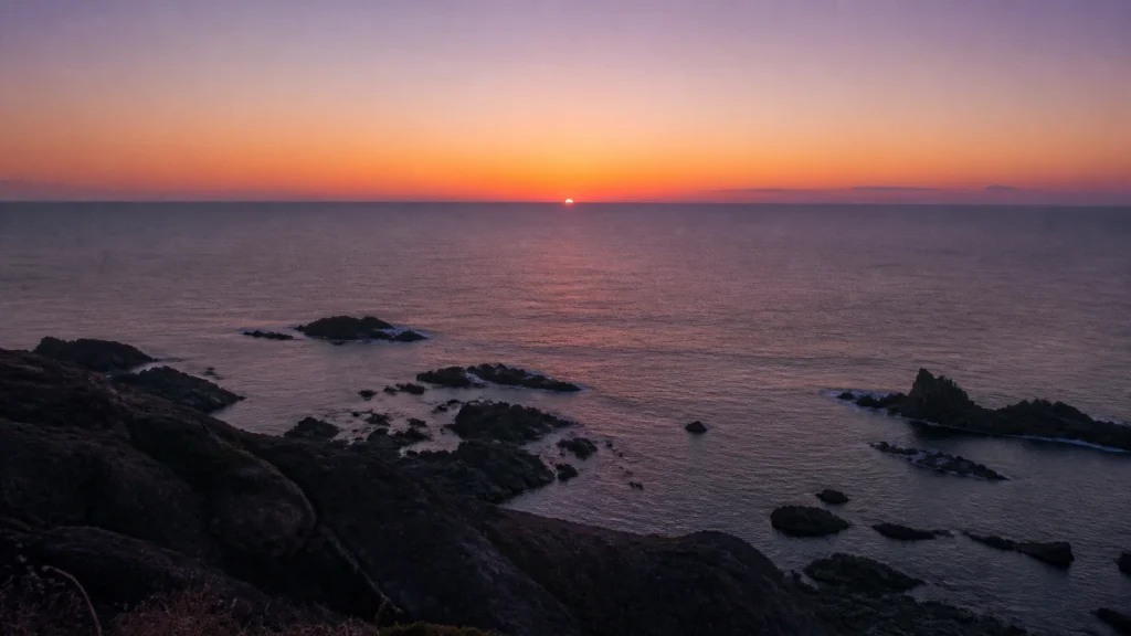 岩礁の海岸越しに、日本海の水平線へ沈もうとする夕日
