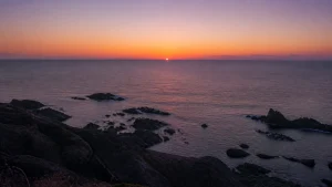 岩礁の海岸越しに、日本海の水平線へ沈もうとする夕日