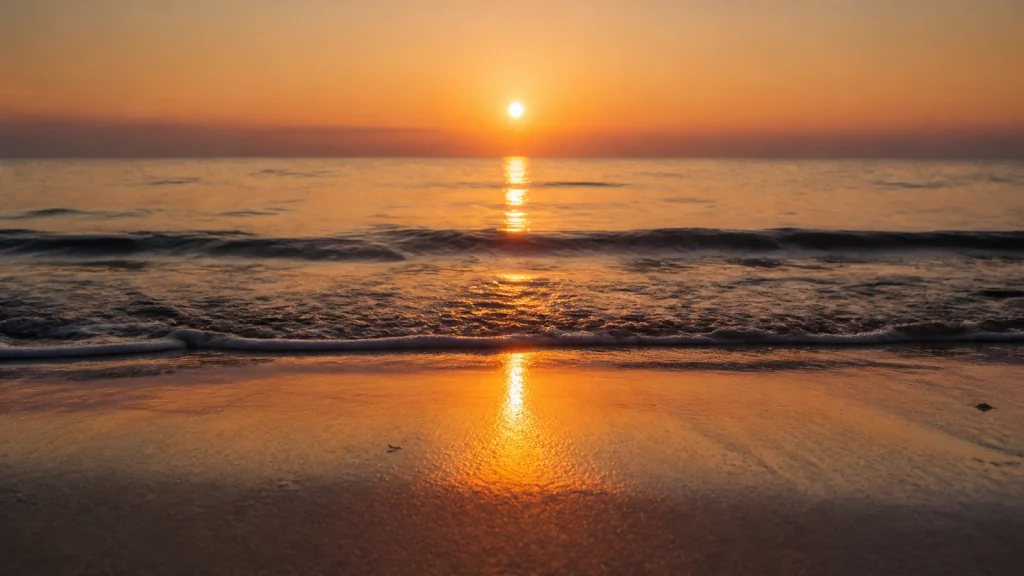 砂浜から見た、海面に一本の道のように伸びる夕日の光
