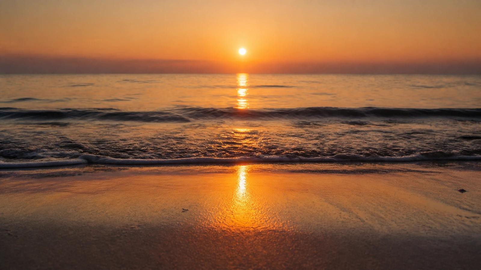 砂浜から見た、海面に一本の道のように伸びる夕日の光