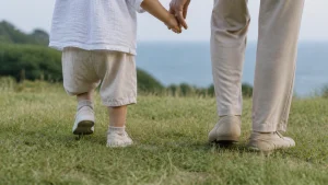 芝生の上で手をつないで歩く、小さな子どもと大人の足元