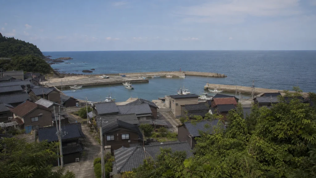 丘の上から見下ろした、瓦屋根の家並みと小さな漁港、その先に広がる日本海